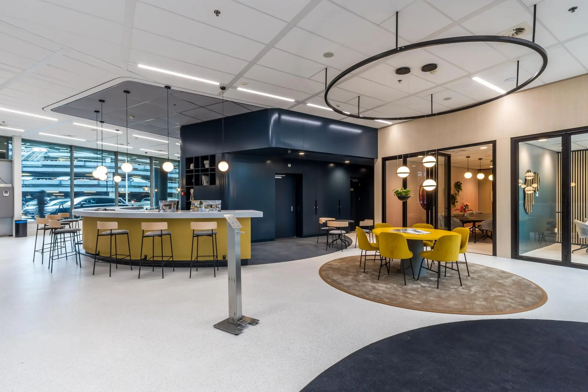 Modern ingerichte kantoorlobby aan de Vliegend Hertlaan met een open zithoek, geel meubilair en een centraal gelegen koffiebar.